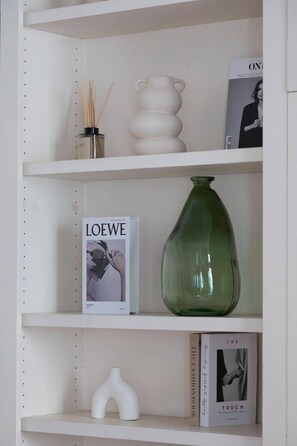 Uma estante com diversos objetos, incluindo uma revista, um vaso verde, um vaso branco e uma pequena escultura branca.