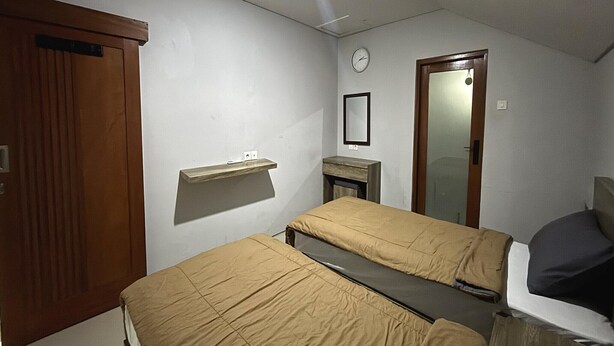 Ein Schlafzimmer mit zwei Betten, einem Holzschrank, einem Spiegel und einer Uhr an der Wand.