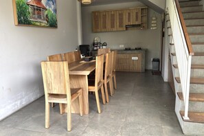 Een eetgedeelte met een houten tafel en stoelen, een keuken met houten kastjes, en een trap met houten treden.
