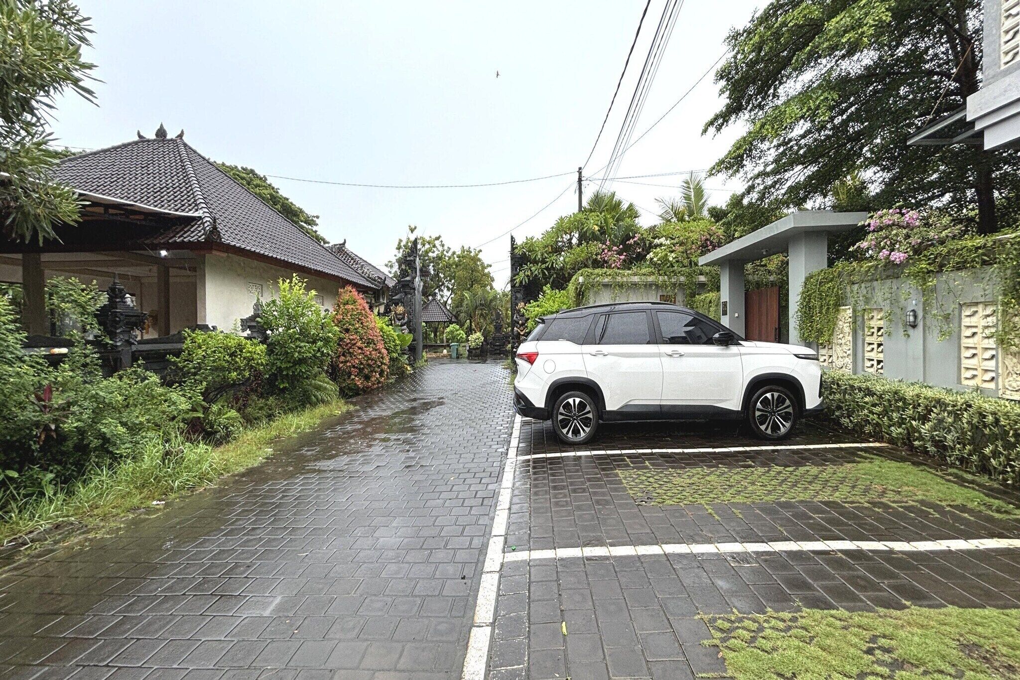 A residential street with a parked white SUV, traditional houses, and lush greenery.