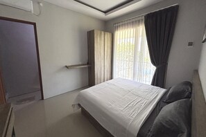 Ein Schlafzimmer mit Bett, Kleiderschrank, einem Fenster mit Vorhängen und einer Tür.