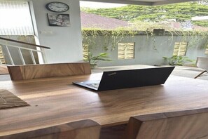 A wooden desk with a laptop, a clock, and a view of greenery outside. - Balcony Suite Near Sanur Beach (Bali)