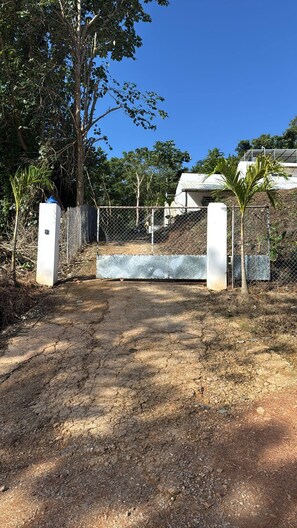 A gated entrance with a dirt path leading to a building, surrounded by trees and a clear sky. - Tranquil Villa Retreat in Las Terrenas - Pet-Friendly Haven (Las Terrenas)