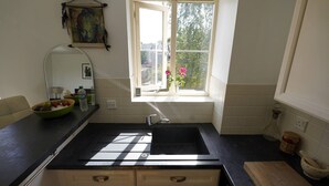 Cozinha com bancada preta, janela com vista para vegetação e uma tigela de frutas no balcão.