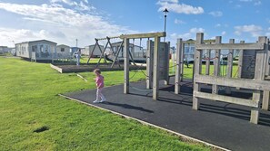Ein Spielplatz mit Holzelementen und einer gepflasterten Fläche.