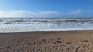 Una spiaggia di ciottoli con onde, cielo sereno e terraferma in lontananza.