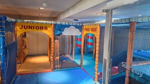 Zona de juegos infantiles con paredes de malla, suelo acolchado y un cartel que indica que es para niños y jóvenes.