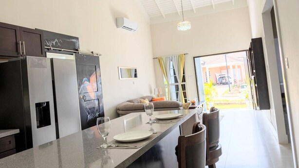 A modern kitchen with a built-in refrigerator, a dining area with a long counter, and a view of the outside. - Beyond Escape-Solar-Powered-3BDRM-Near Ocho Rios (Boscobel)
