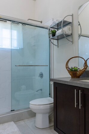 Ein modernes Badezimmer mit Duschkabine aus Glas, einer weißen Toilette und dunklen Schränken.