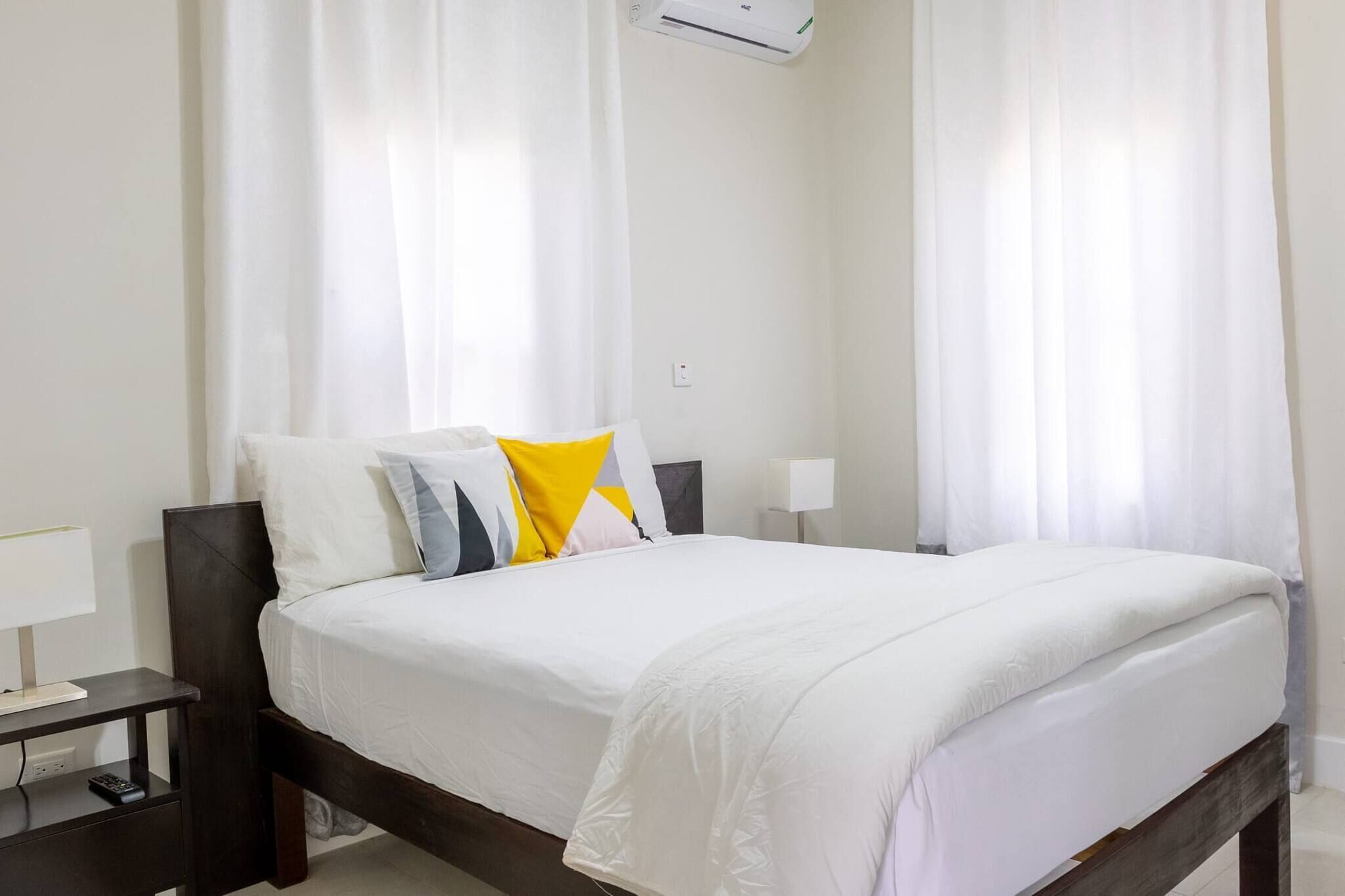 Een hotelkamer met een bed, nachtkastje, lamp en airconditioning.