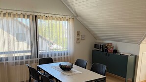 A dining area with a table and chairs, a kitchen area with appliances, and a window with curtains. - Nordi Living Apartment—ideally located in the heart of Baden-Württemberg (Horb am Neckar)
