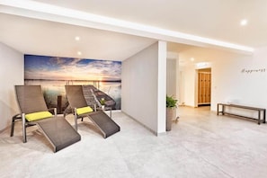 Una habitación moderna con un mural de atardecer, dos sillones de descanso, un banco y una pared con la palabra 'Happiness'.