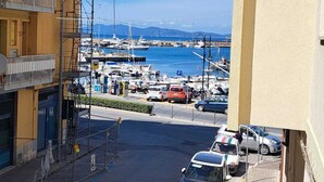 Et gadesyn med parkerede biler, en havn med både og en bygning med balkon.