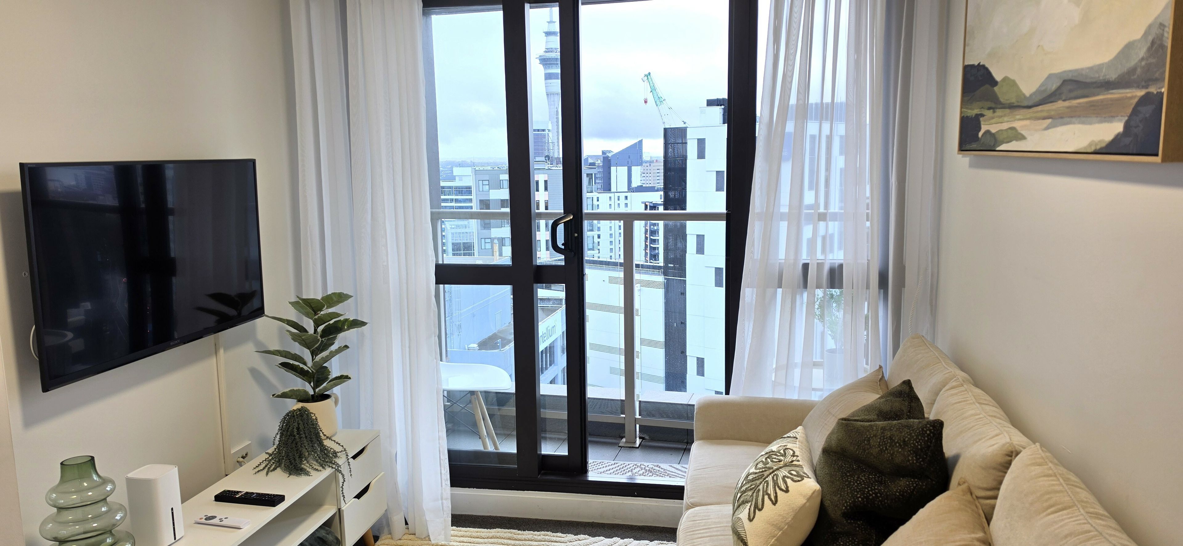 Ein modernes Wohnzimmer mit großem Fenster, einem Flachbildfernseher, einer Couch und einer Topfpflanze.