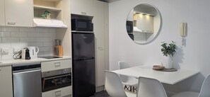 A compact kitchen with a black refrigerator, a microwave, a coffee maker, and a sink. There is a dining table with chairs and a mirror on the wall. - Immaculate 2BDR Central City Chic Apartment (Auckland)