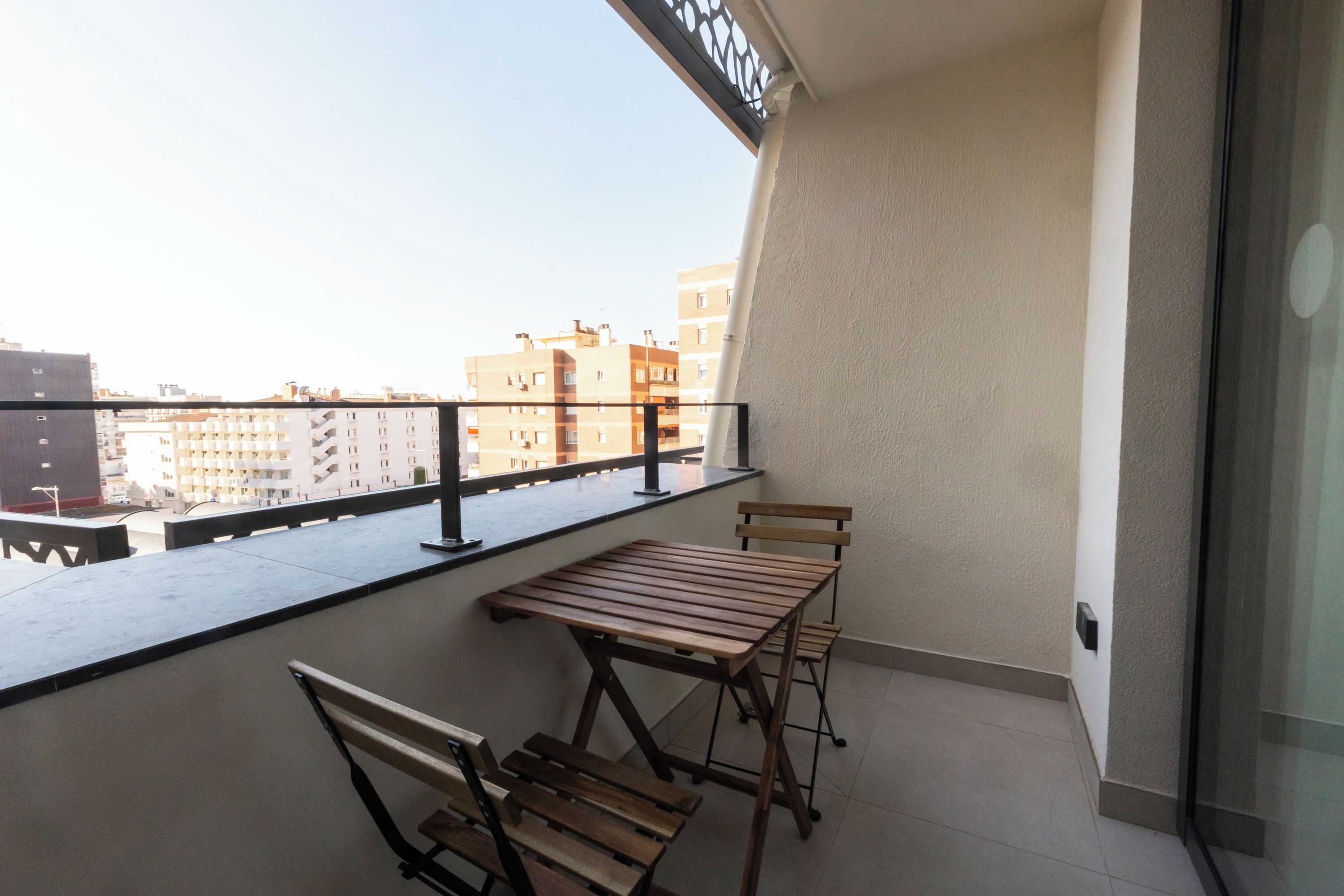 Een balkon met een houten tafel en stoelen, een leuning en uitzicht op gebouwen.