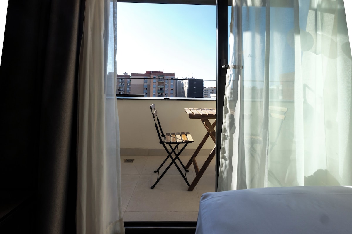 En balkon med et bord og stole, med udsigt over bybilledet.