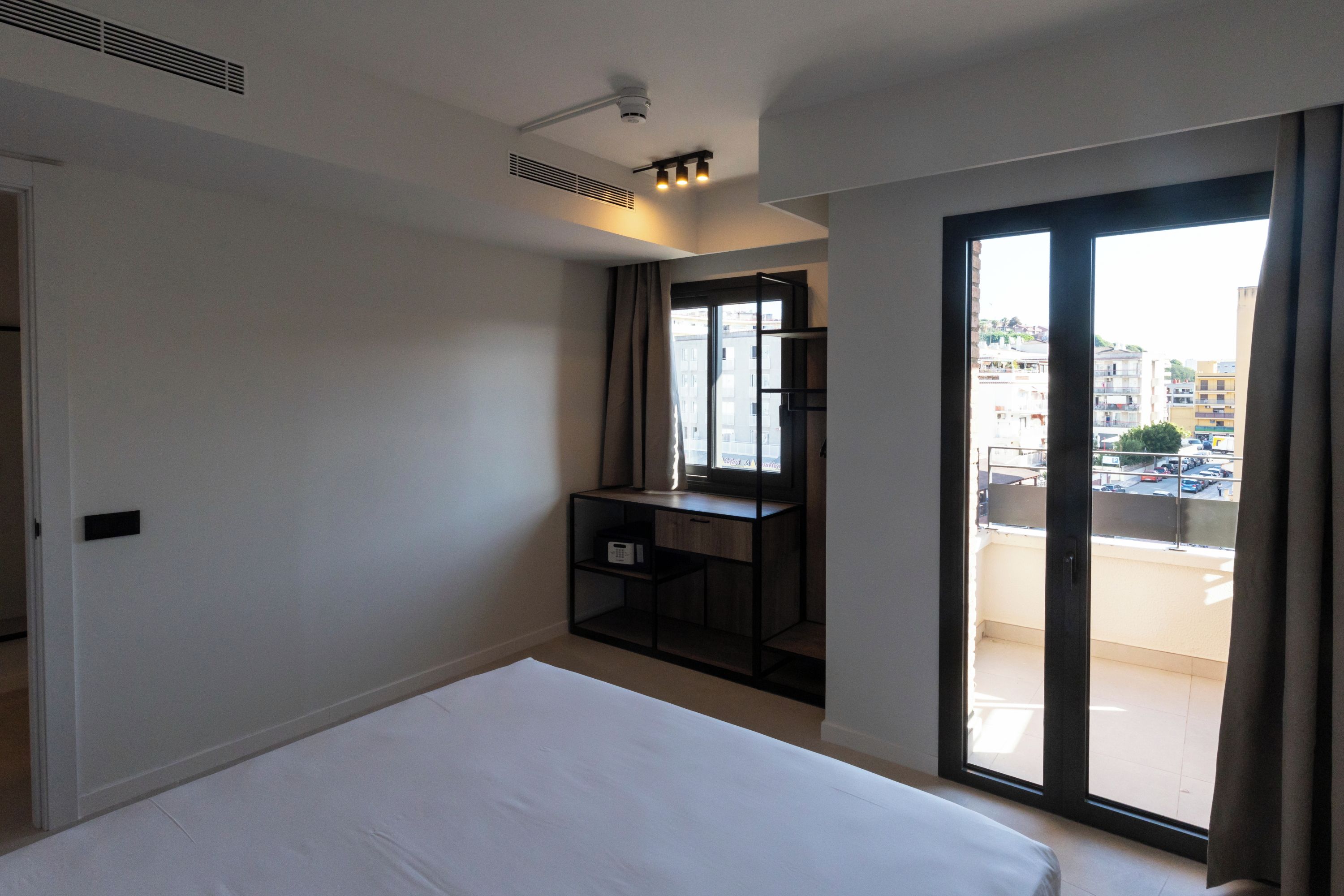 Une chambre d’hôtel comprenant un lit, un bureau, une fenêtre donnant sur la ville et une porte coulissante menant au balcon.
