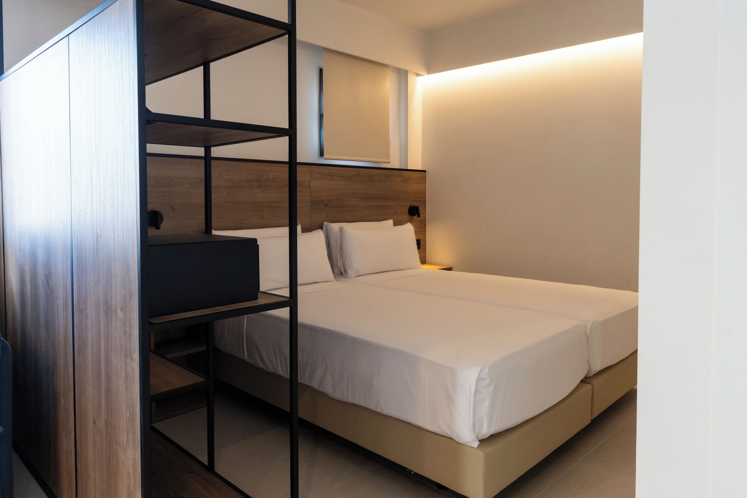 A single bed with a wooden headboard, a built-in shelf unit, and a bedside table.