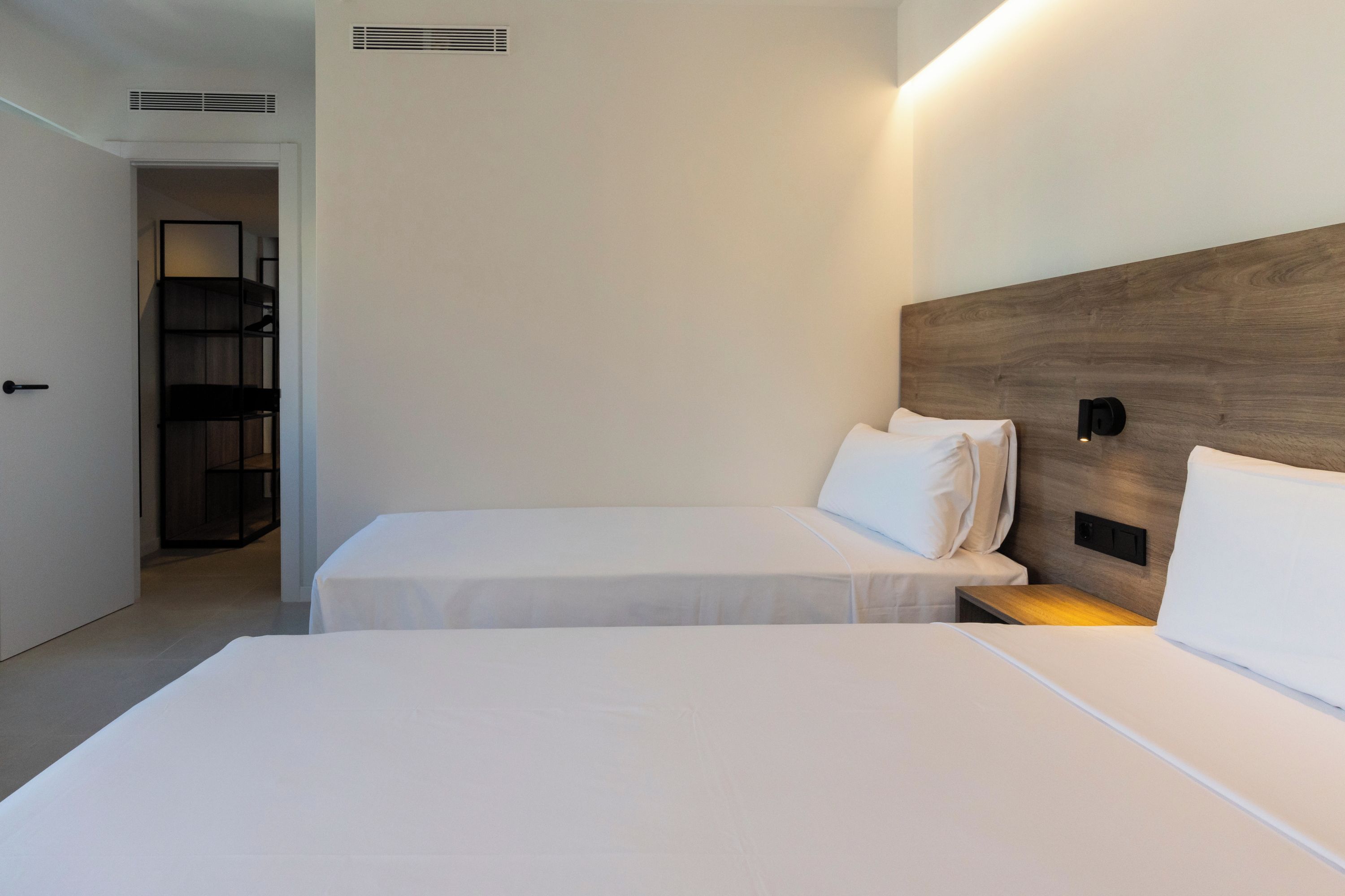 A hotel room with two single beds, a wooden headboard, a bedside table, and a wardrobe.