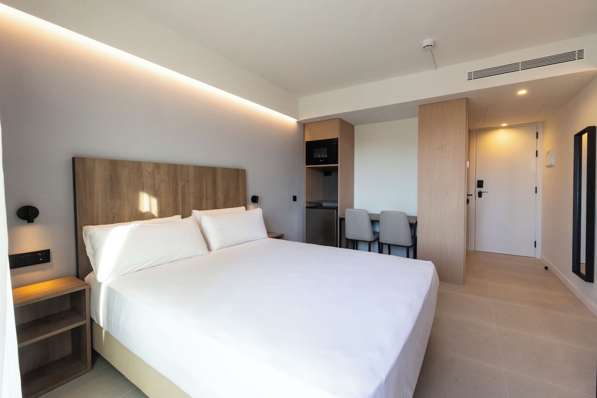 Et moderne hotelværelse med en stor seng, et natbord, en indbygget garderobe og et lille tekøkken.