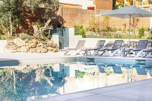Un área de piscina con sillones reclinables y un muro de piedra.