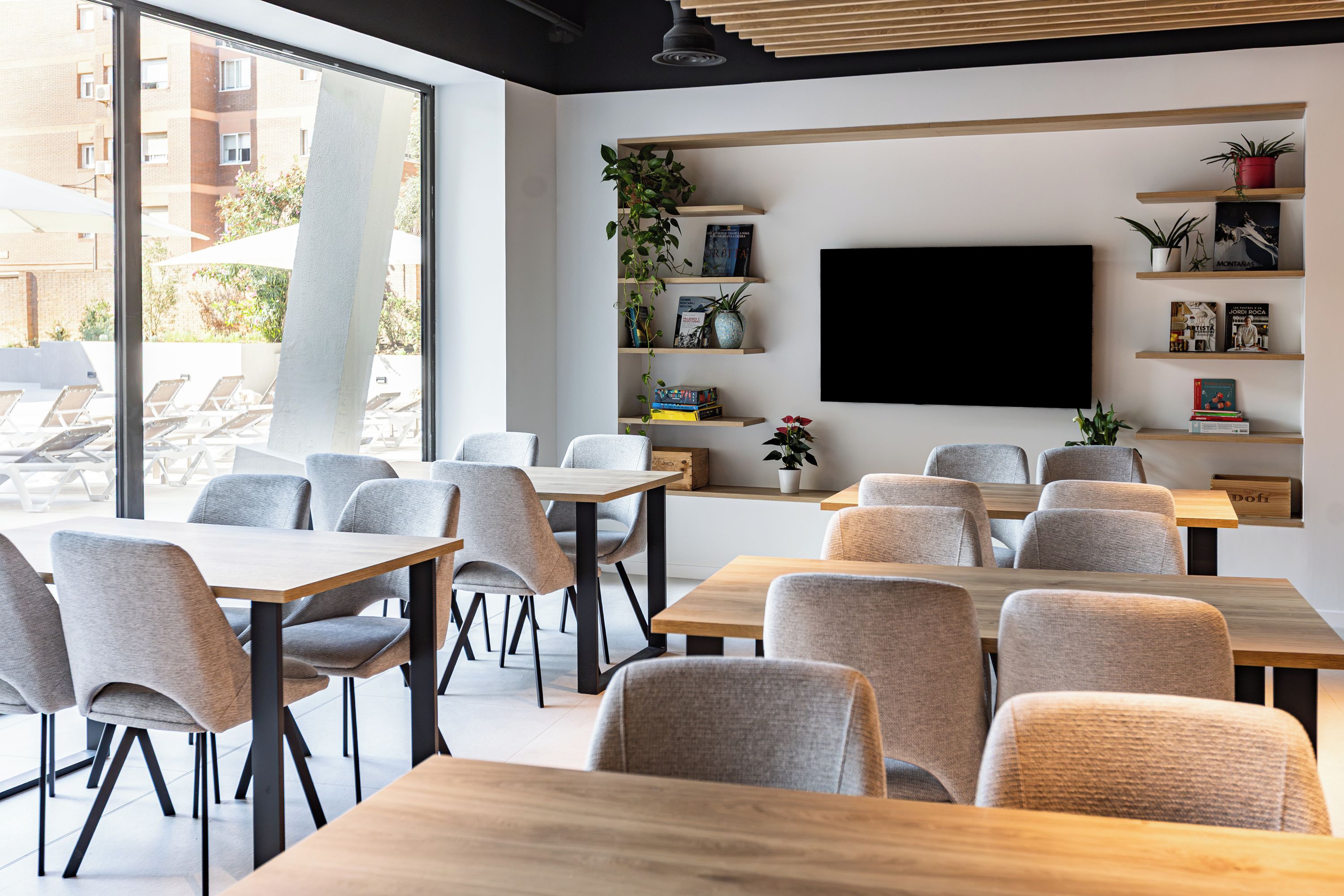 Um café moderno com várias mesas e cadeiras, uma janela ampla e uma televisão na parede.