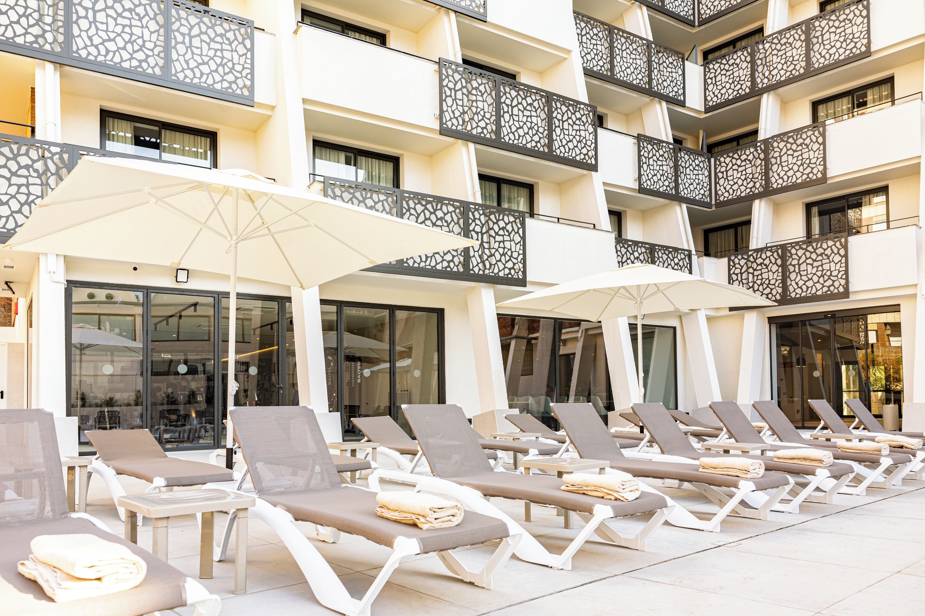 Een hotel met meerdere balkons, ligbedden en parasols.