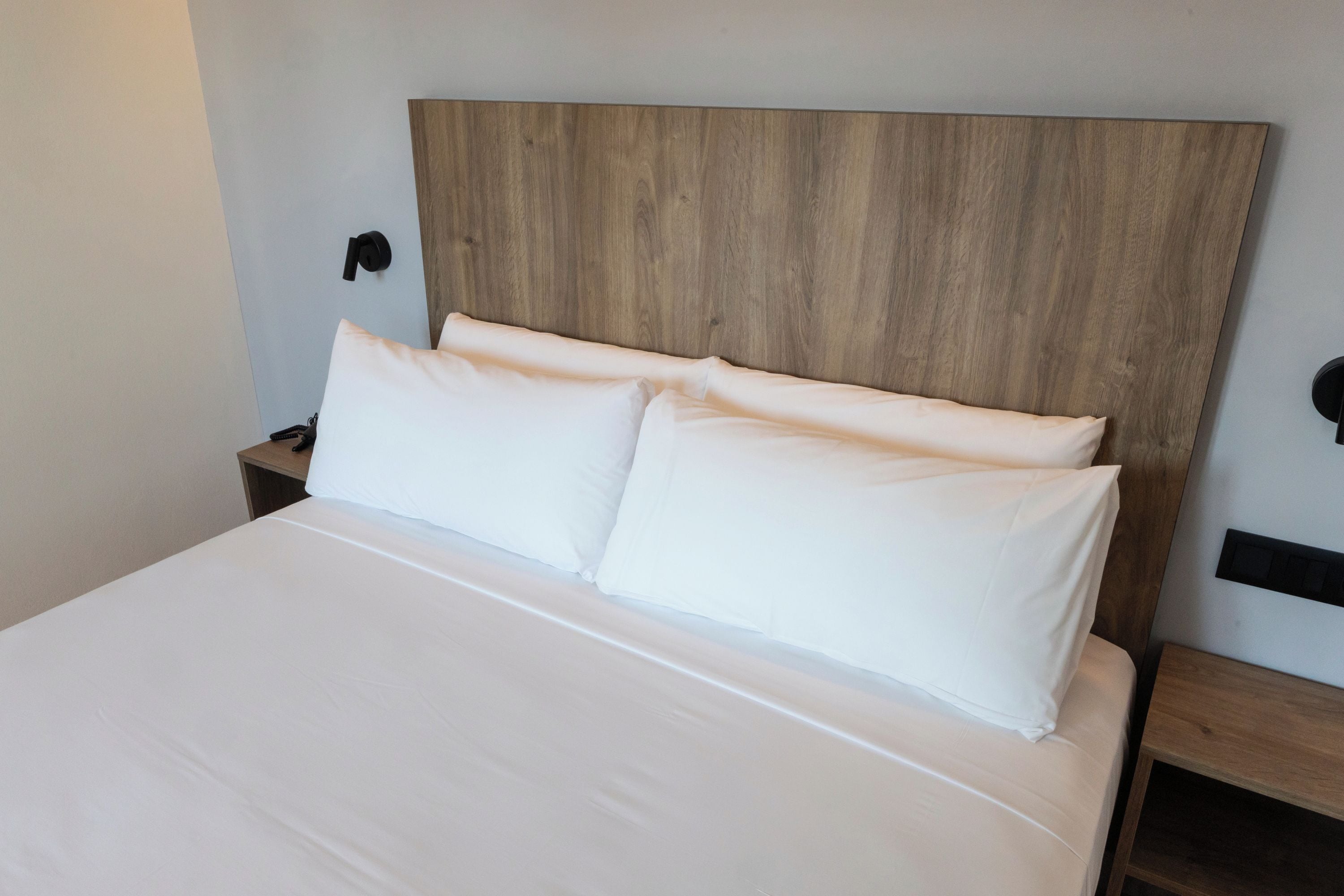 A bed with white linens, a wooden headboard, and two bedside tables with black wall-mounted lamps.
