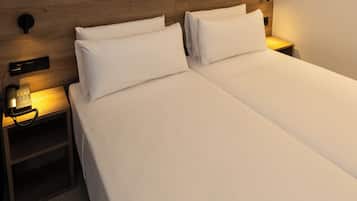 Un lit double bien fait, avec du linge de lit blanc, un téléphone sur la table de chevet et une petite table de nuit en bois.