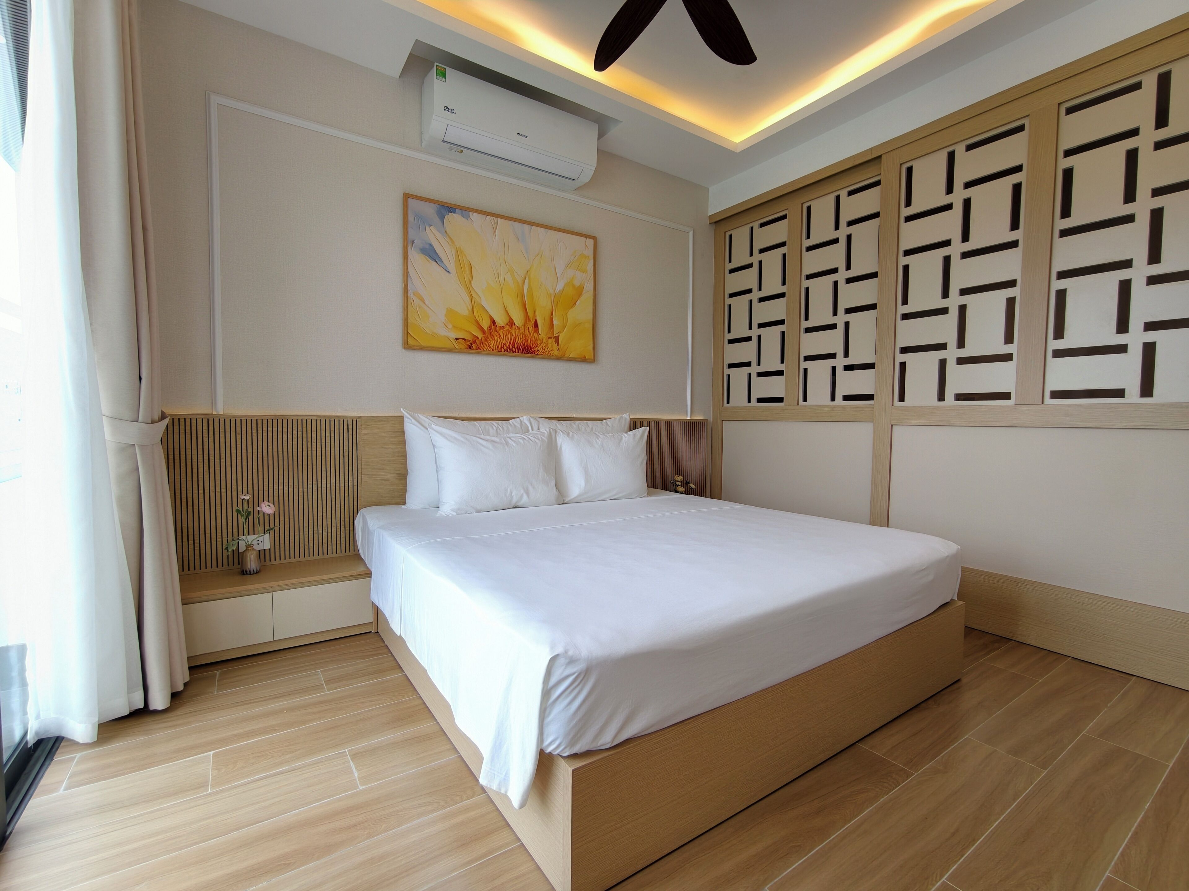 Une chambre d’hôtel comprenant un lit, un climatiseur fixé au mur, un panneau décoratif mural et une fenêtre avec des rideaux.