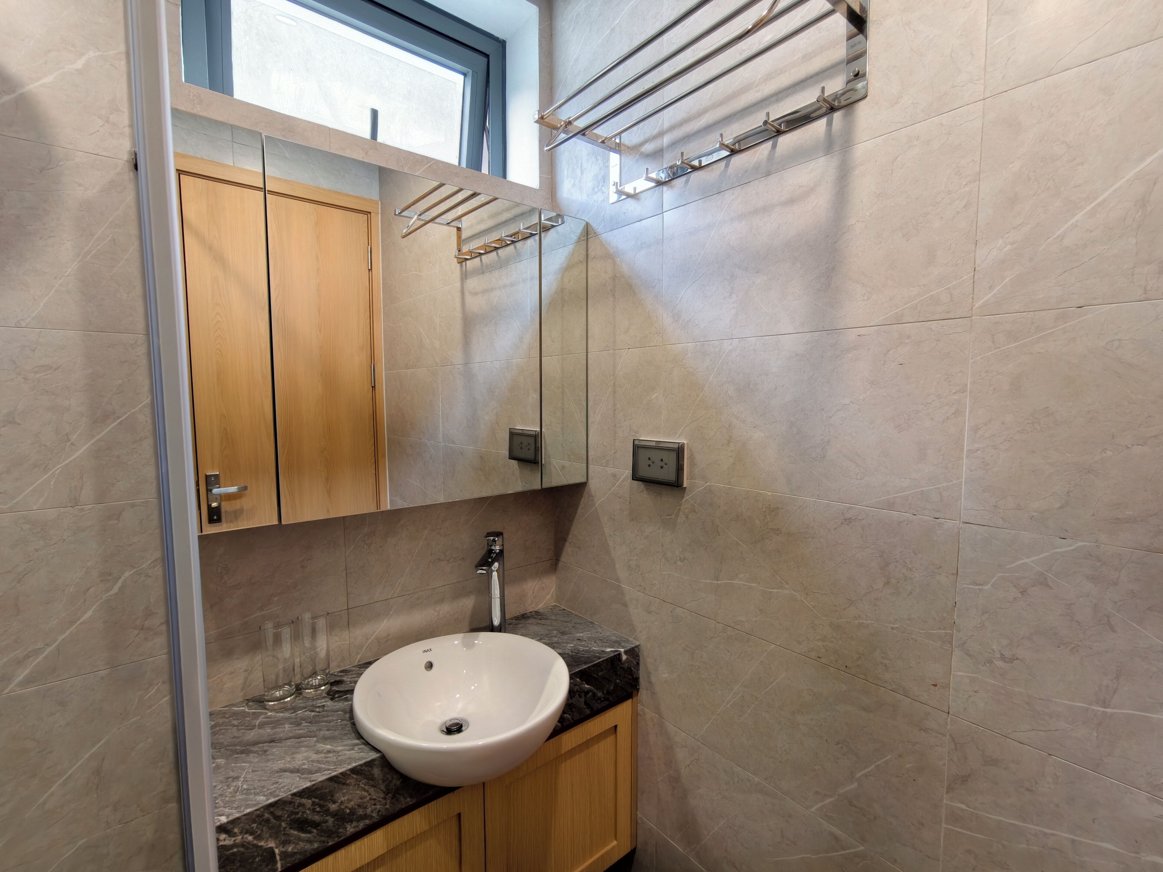 A bathroom with a marble sink, wooden cabinets, a towel rack, and a window.