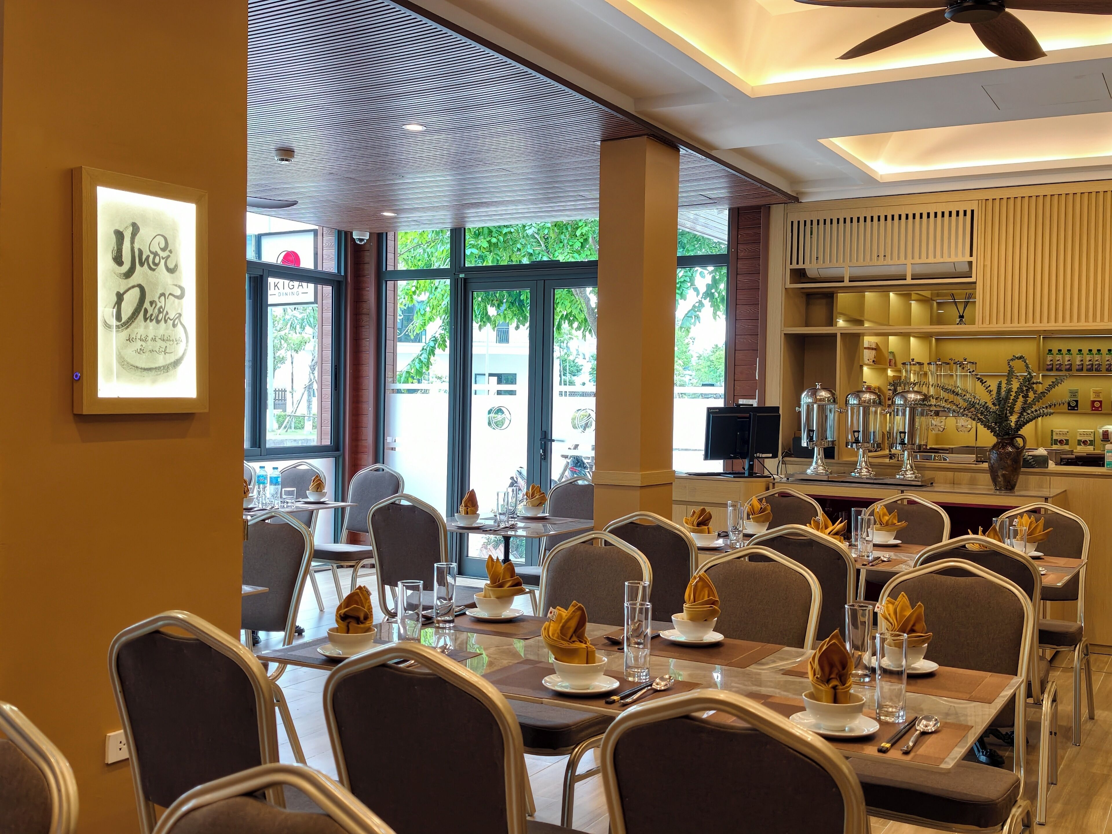 A restaurant interior with tables set for dining, a ceiling fan, and a view of the outdoors.