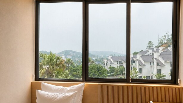 Une chambre à coucher comprenant un lit, un bureau et donnant sur un quartier résidentiel grâce à de grandes fenêtres.