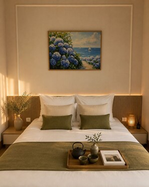 Habitación de hotel ordenada con cama, mesitas de noche, una mesita auxiliar, bandeja con juego de té y un cuadro enmarcado sobre la cama.