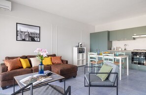 A modern living room with a sofa, coffee table, and a dining area with chairs and a table. - Mondello Bay - Roosevelt Apartments (Palermo)