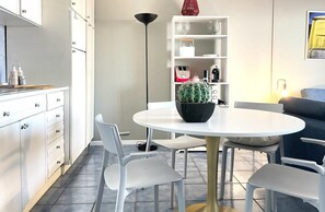 A modern kitchen with white cabinets, a round dining table, and a potted plant. - Mondello Bay - Roosevelt Apartments (Palermo)