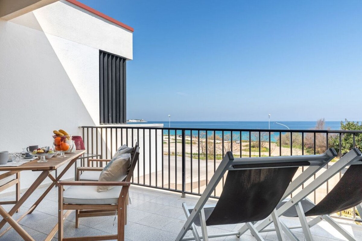 A balcony with a table set for breakfast, a chair, and a view of the sea.