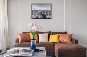 A living room with a brown sofa, a vase with flowers, a book, and a camera on a coffee table. - Mondello Bay - Roosevelt Apartments (Palermo)