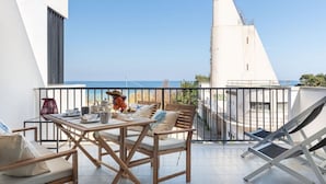 Een balkon met een eettafel, een stoel en een lounge stoel, met uitzicht op de kust.