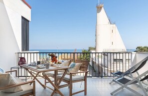 A balcony with a table set for dining, a chair, and a lounge chair, overlooking a coastal view. - Mondello Bay - Roosevelt Apartments (Palermo)