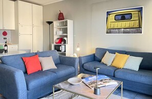 A living room with two blue sofas, a coffee table, a bookshelf, and a framed picture on the wall. - Mondello Bay - Roosevelt Apartments (Palermo)