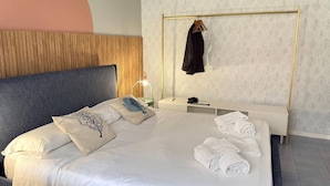 Een net opgemaakt bed met kussens, een nachtkastje met een lamp, en een kapstok.