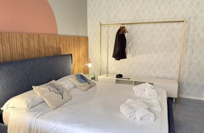 A neatly made bed with pillows, a bedside table with a lamp, and a hanging coat rack. - Mondello Bay - Roosevelt Apartments (Palermo)