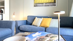 Een woonkamer met een blauwe bank, een bijzettafeltje met een boek, en een vloerlamp.