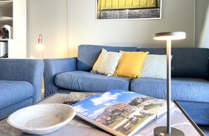 A living room with a blue sofa, a coffee table with a book, and a floor lamp. - Mondello Bay - Roosevelt Apartments (Palermo)