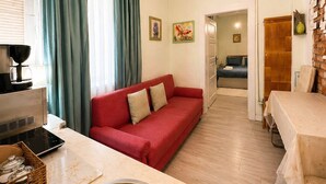 Ett kompakt bostadsutrymme med ett litet kök, en röd soffa, ett matbord och en duschhörna.