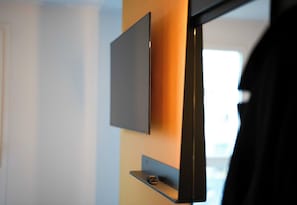 Ein modernes Zimmer mit einem an der Wand montierten Flachbildfernseher, einer kleinen Ablage darunter und einer Tür mit schwarzem Rahmen.