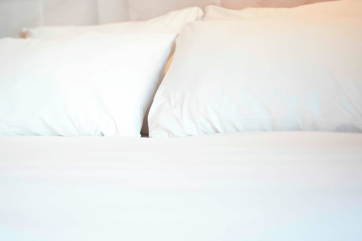 Ein Bett mit weißer Bettwäsche und Kissen.