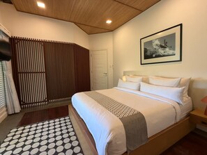 Une chambre d’hôtel avec un lit, un tapis à motifs, un plafond en bois, une porte et un tableau encadré au mur.
